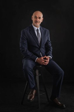 Orta yaşlı, takım elbiseli ve izole edilmiş siyah arka planda oturan bir adam. Boşluğu kopyala. 