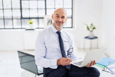 Ofiste elinde dizüstü bilgisayarla duran bir iş adamı. Takım elbiseli ve kravatlı orta yaşlı profesyonel bir adam..