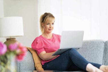 Sarışın kadın evde oturuyor ve iş için dizüstü bilgisayar kullanıyor. Sıradan kıyafetler giyen orta yaşlı bir kadın.. 