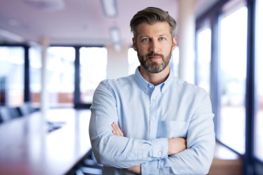 Konferans odasında kollarını kavuşturmuş orta yaşlı bir adamın portresi..  