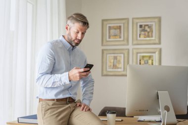 Evde oturup akıllı telefon ve bilgisayar kullanan kendine güvenen bir adam. Orta yaşlı iş adamı mesajları. Merkez Ofis. 