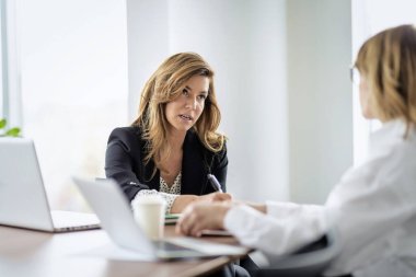 Bir grup iş kadını masada oturuyor ve iş toplantısı yapıyorlar. Modern bir ofiste takım çalışması..