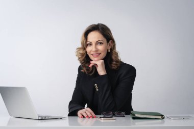 Orta yaşlı bir iş kadını, izole edilmiş beyaz arka planda masa başında oturuyor. İş için dizüstü bilgisayar kullanan kendine güvenen profesyonel bir kadın. Boşluğu kopyala.