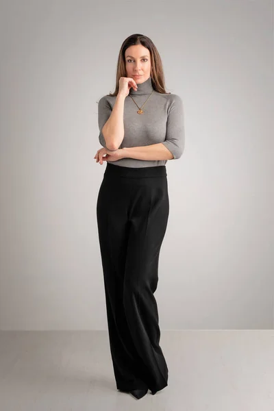 隔離された背景に対してタートルネックセーターと黒いズボンを身に着けている魅力的な中年の女性の全長 コピースペース ロイヤリティフリーのストック画像
