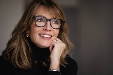 İçeride oturan çekici, sarı saçlı bir kadının yakın plan fotoğrafı. Siyah kazak ve gözlük takan orta yaşlı bir kadın.. 