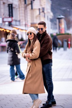 Sokakta yürüyen ve birbirini kucaklayan mutlu bir çiftin uzunluğu. Esmer, şapka ve ceket giyen kadın ve güneş gözlüğü ve ceket giyen yakışıklı adam..