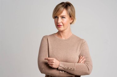 Çekici, orta yaşlı bir kadının portresi kolları kapalı, gri arka planda duruyor. Boşluğu kopyala. 