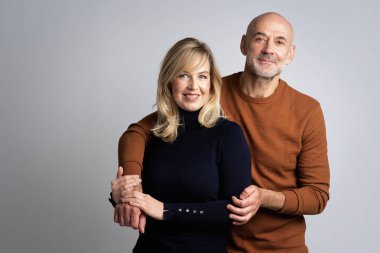 Sarışın kadın ve gülümseyen orta yaşlı adam soyutlanmış arka planda yan yana duruyorlar. Orta yaşlı çift kameraya bakıyor ve neşeli bir şekilde öpüşüyorlar. Boşluğu kopyala.