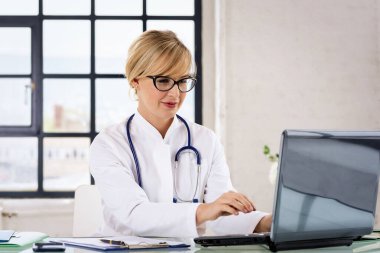 Gülümseyen kadın sağlık çalışanı dizüstü bilgisayar kullanıyor ve doktor odasında çalışıyor.. 