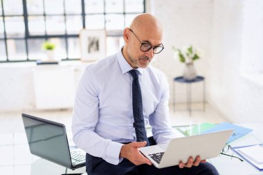 Ofiste elinde dizüstü bilgisayarla oturan bir iş adamı. Orta yaşlı profesyonel bir adam gömlek ve kravat takıyor ve internet konferansı yapıyor..