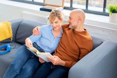 Orta yaşlı bir çift evdeki kanepede oturup kitap okuyor. Sarışın kadın ve orta yaşlı adam günlük kıyafetler giyip evde dinleniyorlar..
