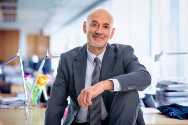Orta yaşlı bir işadamı ofisinde oturuyor. Takım elbiseli ve kravatlı kendine güvenen profesyonel bir adam.. 