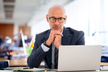 Ofiste oturan orta yaşlı bir işadamı ve not defterini iş için kullanıyor. Kendine güvenen, takım elbiseli, kravatlı ve defterine özenle bakan profesyonel bir adam..  