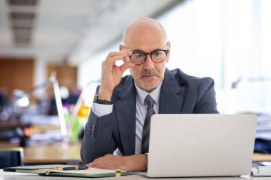 Ofiste oturan orta yaşlı bir işadamı ve not defterini iş için kullanıyor. Kendine güvenen, takım elbiseli, kravatlı ve defterine özenle bakan profesyonel bir adam..  
