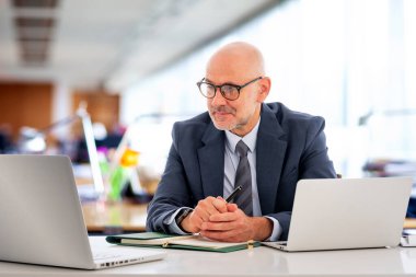 Ofiste oturan orta yaşlı bir işadamı ve not defterini iş için kullanıyor. Kendine güvenen, takım elbiseli, kravatlı ve defterine özenle bakan profesyonel bir adam..  