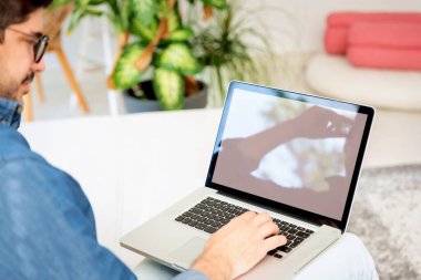 Bilgisayarını kullanan bir adamın arka görüntüsü. Orta yaşlı erkek, günlük giysiler giyiyor ve laptopuyla evde çalışıyor..