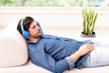 Kulaklığı elinde, evdeki kanepede uzanıp müzik dinleyen bir adamın yakın çekimi.. 