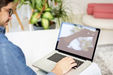 Bilgisayarını kullanan bir adamın arka görüntüsü. Orta yaşlı erkek, günlük giysiler giyiyor ve laptopuyla evde çalışıyor..