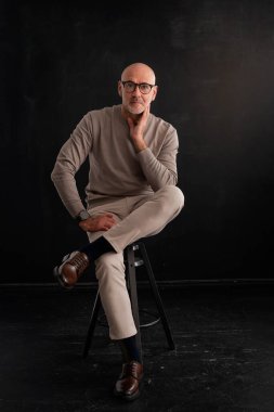 Tecrit edilmiş siyah arka planda olgun bir adamın portresi. Kendine güvenen erkek balıkçı yaka kazak giyiyor. Tam boy çekim.