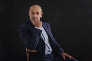 Ciddi yüzlü iş adamının takım elbise giyip izole edilmiş gri arka planda oturduğu görüntüler. Boşluğu kopyala.