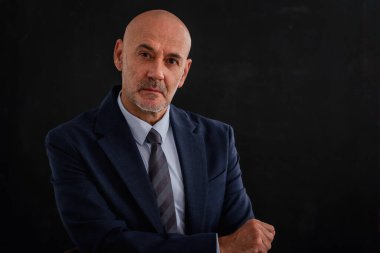 Takım elbiseli, kravatlı ve gri arka planda oturan ciddi yüzlü iş adamının görüntüsü. Boşluğu kopyala.