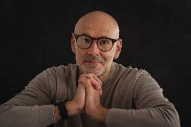 Tecrit edilmiş siyah arka planda olgun bir adamın portresi. Gözlüklü ve balıkçı yaka kazaklı kendinden emin bir erkek. Boşluğu kopyala. 