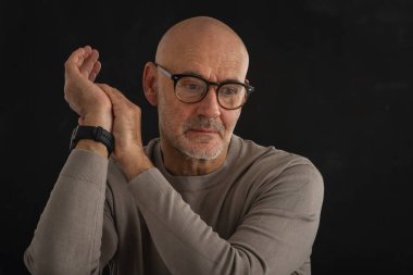 Gözlüklü olgun bir adamın portresi izole edilmiş siyah arka plana dikkatlice bakıyor. Balıkçı yaka kazak giyen kendinden emin bir erkek..