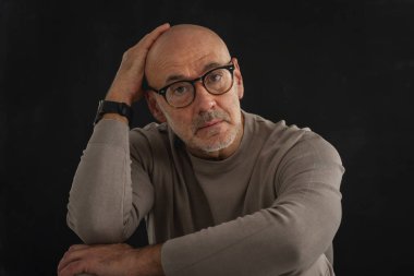 Gözlüklü olgun bir adamın portresi izole edilmiş siyah arka plana dikkatlice bakıyor. Balıkçı yaka kazak giyen kendinden emin bir erkek..