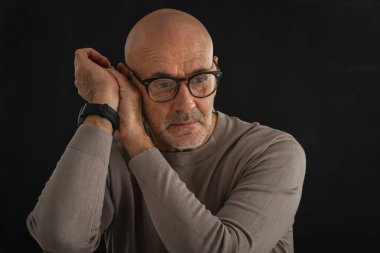 Gözlüklü olgun bir adamın portresi izole edilmiş siyah arka plana dikkatlice bakıyor. Balıkçı yaka kazak giyen kendinden emin bir erkek..