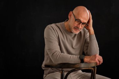 Gözlüklü olgun bir adamın portresi izole edilmiş siyah arka plana dikkatlice bakıyor. Balıkçı yaka kazak giyen kendinden emin bir erkek..