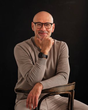 Siyah arka planda orta yaşlı bir adamın stüdyo resmi. Kel ve sakallı bir adam, izole bir arka planda günlük kıyafetler ve gözlük takıyor. Boşluğu kopyala. 