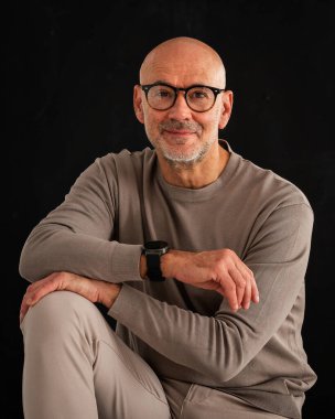Siyah arka planda orta yaşlı bir adamın stüdyo resmi. Kel ve sakallı bir adam, izole bir arka planda günlük kıyafetler ve gözlük takıyor. Boşluğu kopyala. 