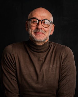 Siyah arka planda orta yaşlı bir adamın stüdyo resmi. Kel ve sakallı bir adam, izole bir arka planda günlük kıyafetler ve gözlük takıyor. Boşluğu kopyala. 