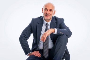 İzole edilmiş beyaz arka planda oturan orta yaşlı bir adam. Takım elbiseli, kravatlı ve kameraya gülümseyen yakışıklı bir adam. Boşluğu kopyala.