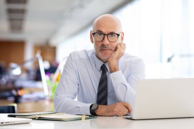 Ofiste oturan orta yaşlı bir işadamı ve not defterini iş için kullanıyor. Gömlek ve kravat takan kendine güvenen profesyonel bir adam..