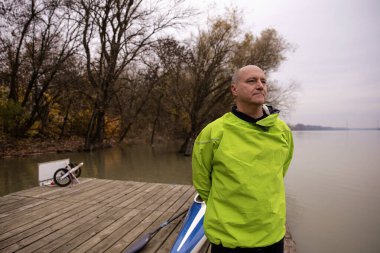 Orta yaşlı, kuru takım elbiseli ve nehir kıyısındaki iskelede duran bir adamın yakın plan portresi..