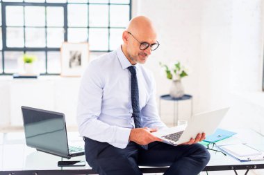 Orta yaşlı bir işadamı ofisinde oturuyor ve çalışıyor. Profesyonel bir adam dizüstü bilgisayar kullanıyor ve video görüşmesi yapıyor.. 