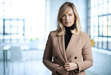 Ofiste kameraya bakarken güzel sarı saçlı bir iş kadınının portresi. Ceket ve kazak giyen kendinden emin bir kadın..