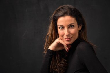 Çekici, orta yaşlı bir kadının izole edilmiş karanlık arka planda oturduğu bir stüdyo portresi. Uzayı kopyala Eller çenede..