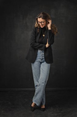 Uzun boylu, kumral bir kadın spor ceket giyiyor ve siyah arka planda kot pantolon giyiyor. Boşluğu kopyala. 