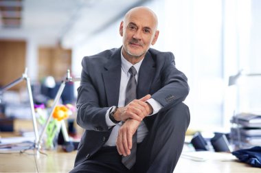 Orta yaşlı bir işadamı ofisinde oturuyor. Takım elbiseli ve kravatlı kendine güvenen profesyonel bir adam.. 