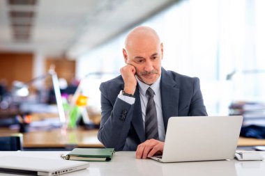 Ofiste oturan orta yaşlı bir işadamı ve not defterini iş için kullanıyor. Kendine güvenen, takım elbiseli, kravatlı ve defterine özenle bakan profesyonel bir adam..  