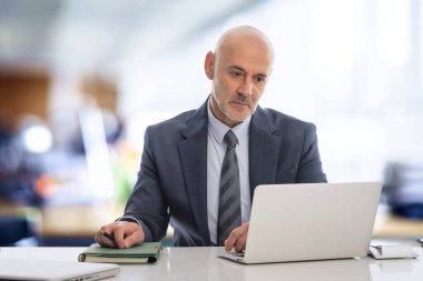 Ofiste oturan orta yaşlı bir işadamı ve not defterini iş için kullanıyor. Kendine güvenen, takım elbiseli, kravatlı ve defterine özenle bakan profesyonel bir adam..  
