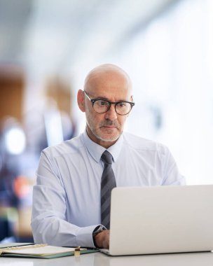 Ofiste oturan orta yaşlı bir işadamı ve not defterini iş için kullanıyor. Gömlek ve kravat takan kendinden emin profesyonel bir adam.. 