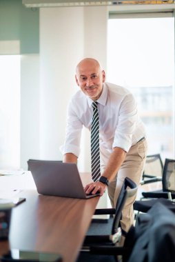Orta yaşlı bir iş adamının ofis masasında dizüstü bilgisayar kullanırken görüntüsü. Modern bir ofiste çalışan profesyonel bir adam..