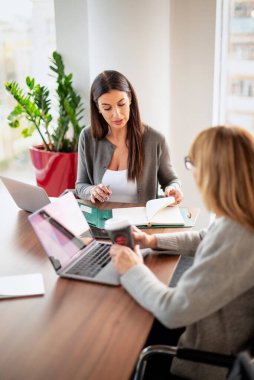 Modern bir ofiste masa başında oturan ve dizüstü bilgisayarlarla çalışan iki iş kadını. Takım çalışması. Bir grup iş adamı toplantı sırasında tartışıyor.