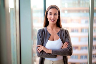 Modern bir ofiste kolları bağlı duran orta yaşlı bir kadın. Çekici iş kadını rahat giyinmiş ve kameraya bakıyor.. 