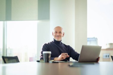  Orta yaşlı iş adamı, modern bir ofis alanında dizüstü bilgisayarda çalışıyor. Gündelik kıyafetler giyen kendinden emin bir erkek.. 