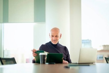  Orta yaşlı iş adamı, modern bir ofis alanında dizüstü bilgisayarda çalışıyor. Gündelik kıyafetler giyen kendinden emin bir erkek.. 