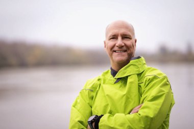 Close-up portrait of middle-aged man wearing dry suit and standing on the jetty by the river. clipart